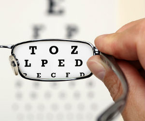 This is a photo of a person holding glasses in front of an eye chart.