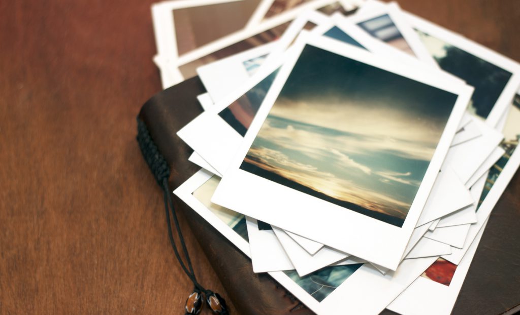 Old polaroid pictures of a sunset piled on top of a leather journal.