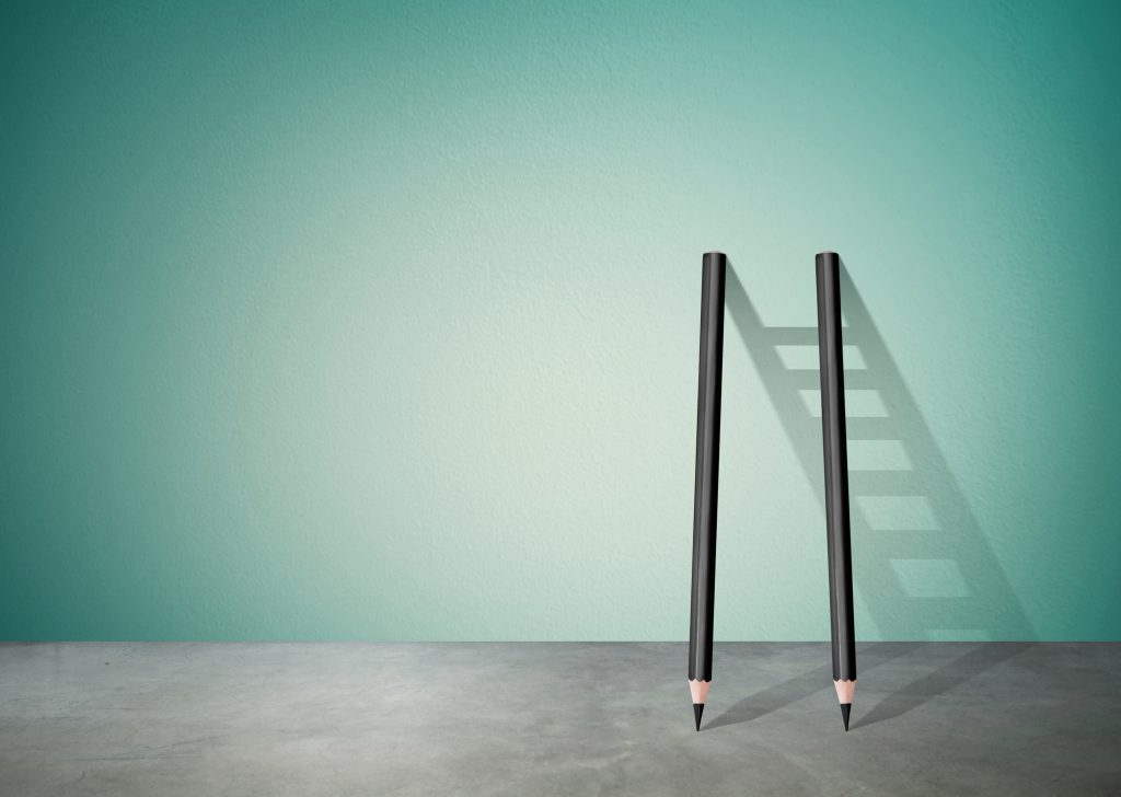 Two pencils propped on wall with ladder shadow