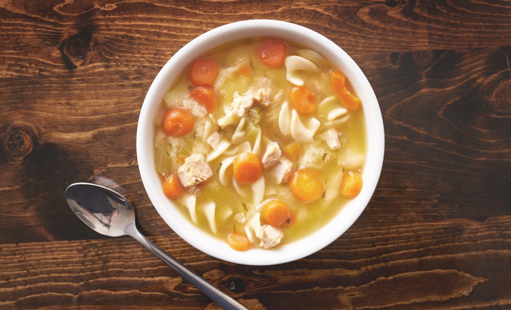 bowl of chicken noodle soup shot top down on wooden table top