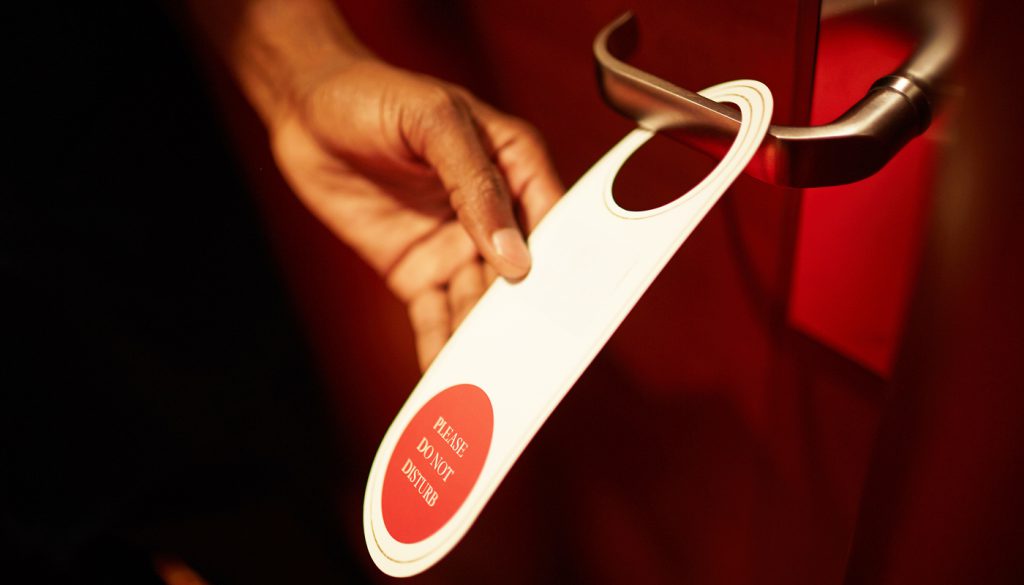 Closeup shot of a person's hand hanging do not disturb sign on doorknob of hotel room