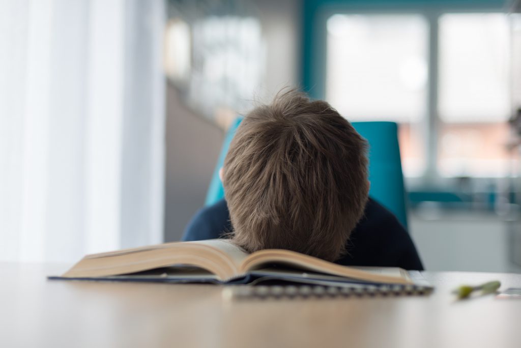 Tired 8 years old boy doing his homework at the table.