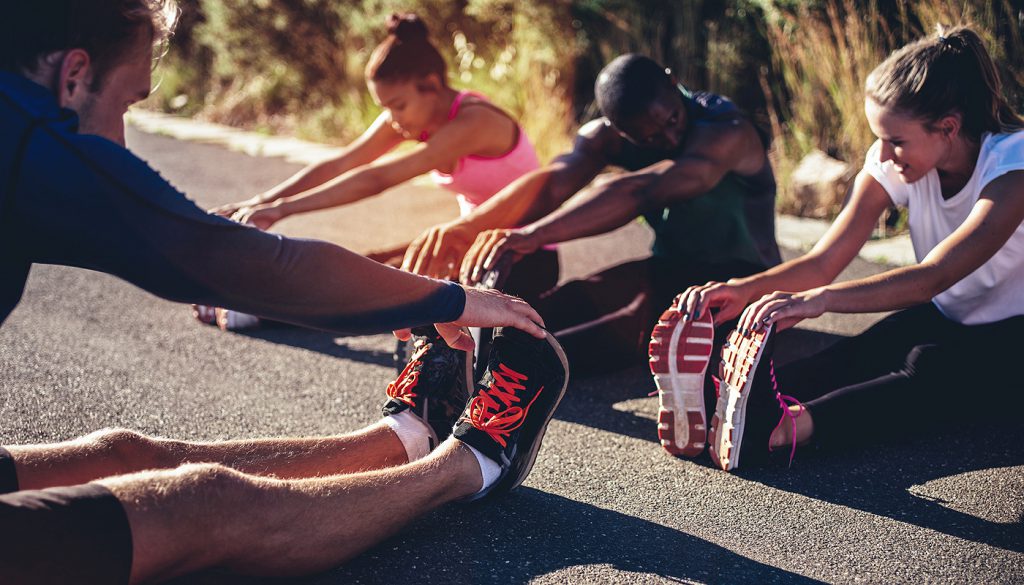 Multi-ethnic group of young adult athletes doing hamstring stretch exercises after a running workout