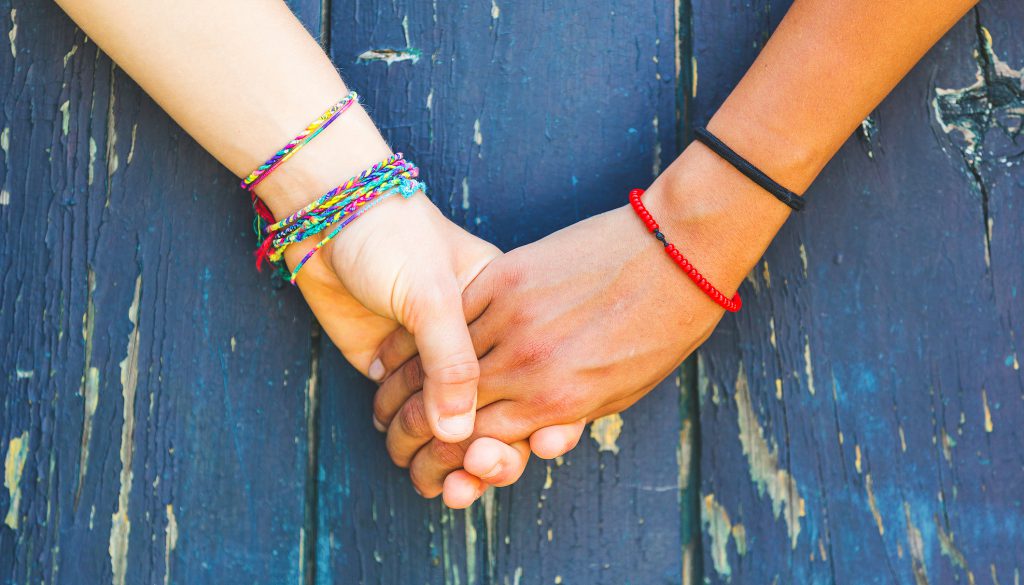 Teens holding hands with a wooden background.