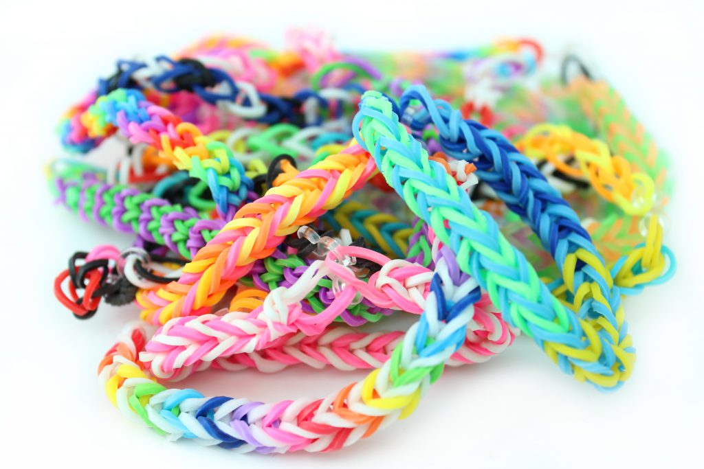 Photo showing a pile of rainbow coloured loom bracelets, made from coloured rubber loom bands. These friendship bracelets are popular with young children, who weave the rubber bands together using a simple plastic loom device.