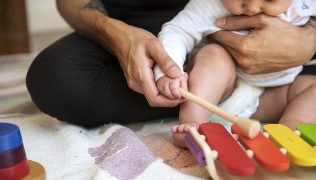 Father showing infant how to play a xylophone