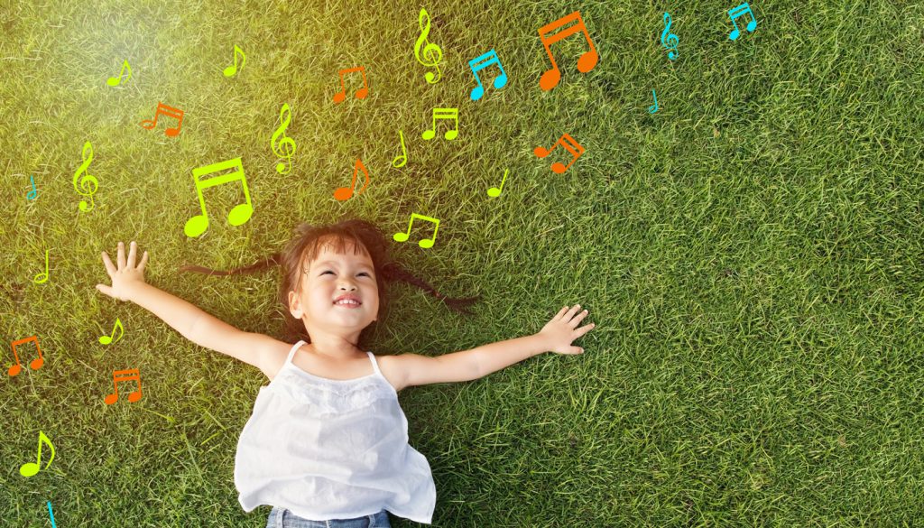 Little girl smiling and lying on grass with music notes around her