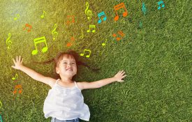 Little girl smiling and lying on grass with music notes around her