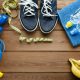 Fitness concept with sneakers dumbbells skipping rope measure tape towel bottle of water and bananas on wooden table background