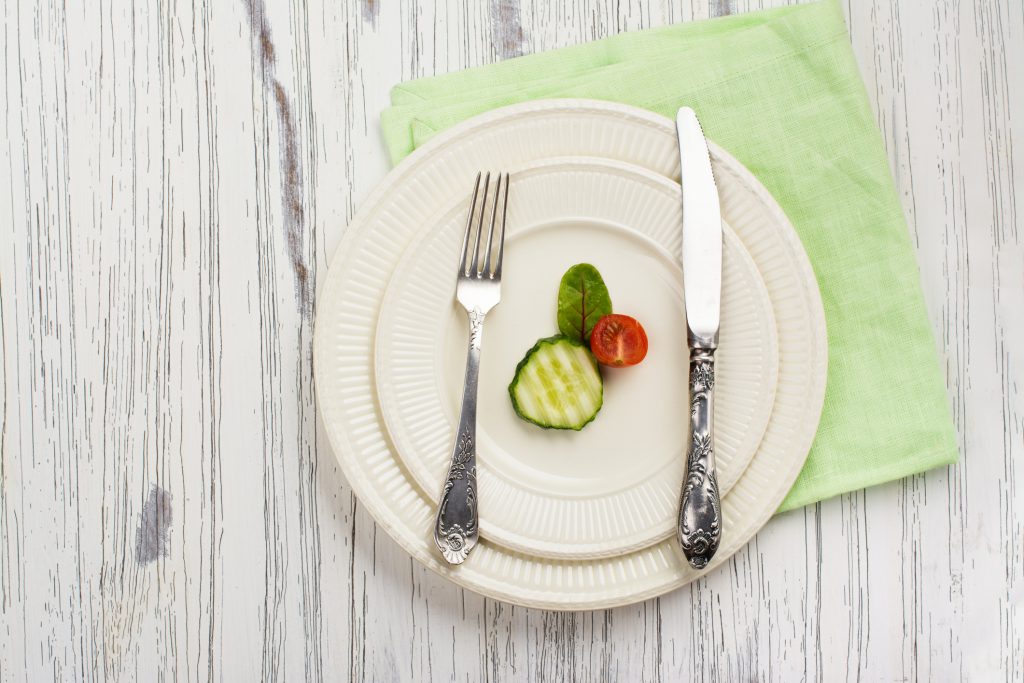 Plate with one slice of cucumber, small tomato, and basil leaf