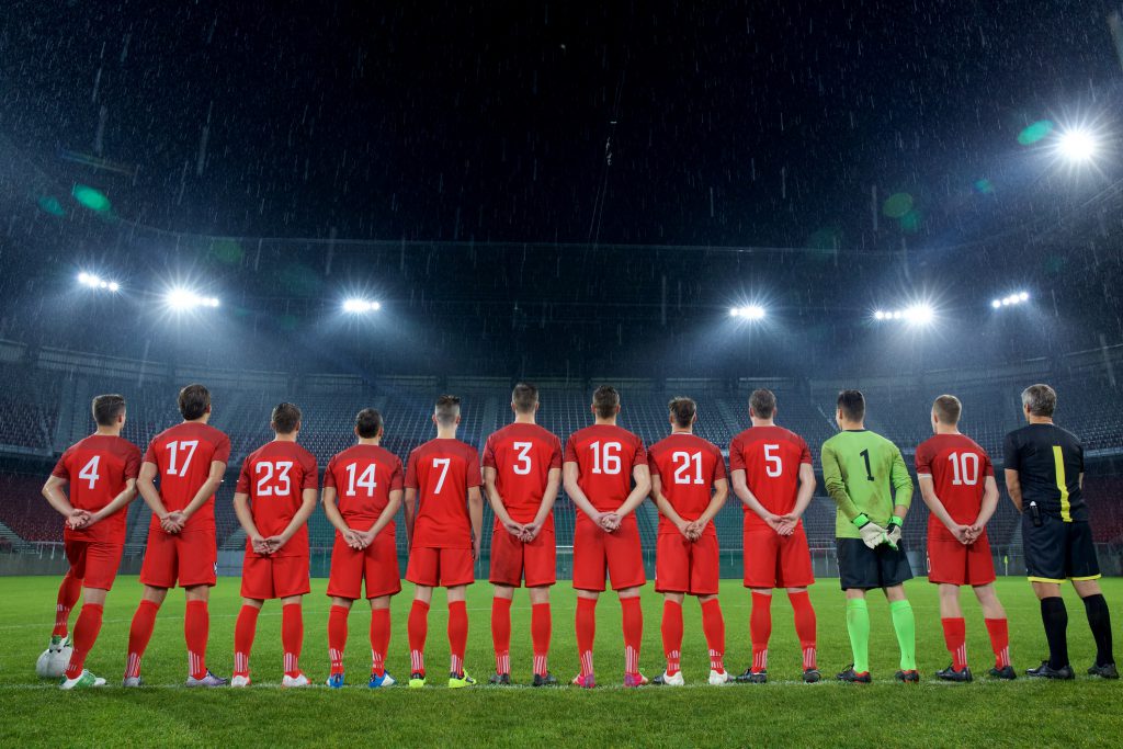 Rear view of football team standing in a row during national anthem before match.