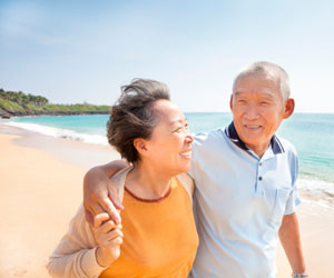 This is a picture of an elderly Asian couple taking a walk on the beach.
