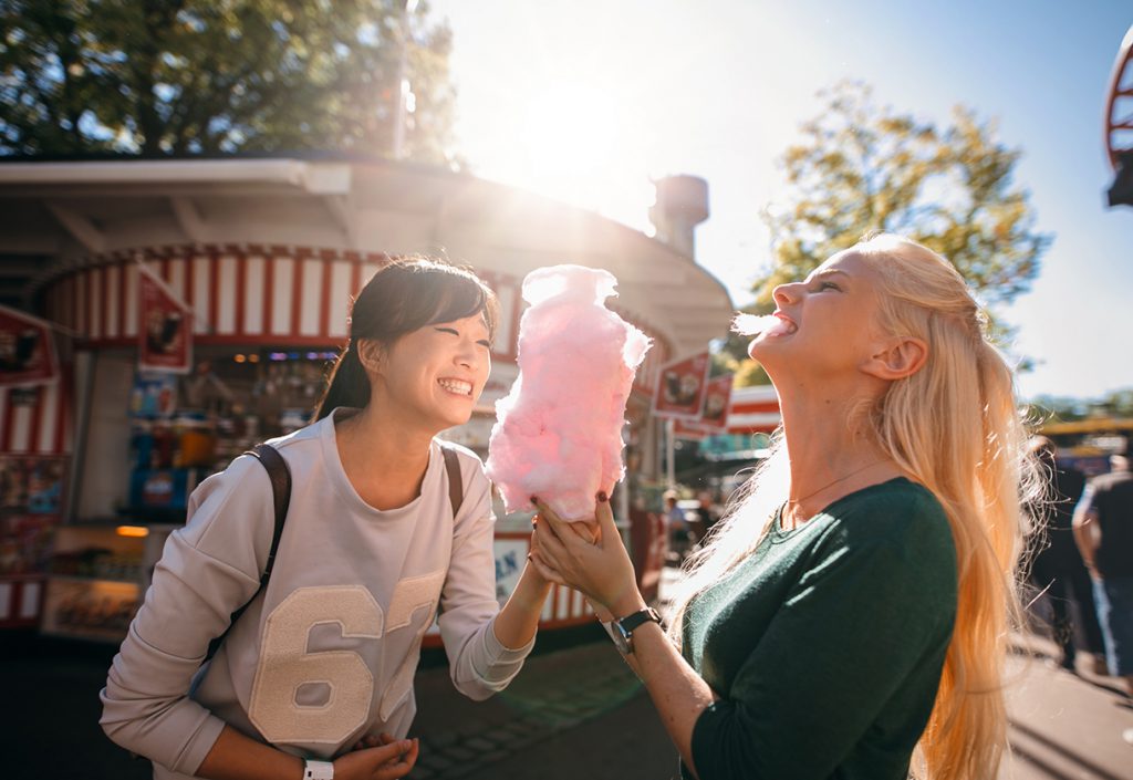 Photo of two young women sharing cotton candy at an amusement park