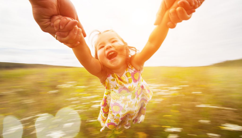 Happy girl spinning around her parent in a field.