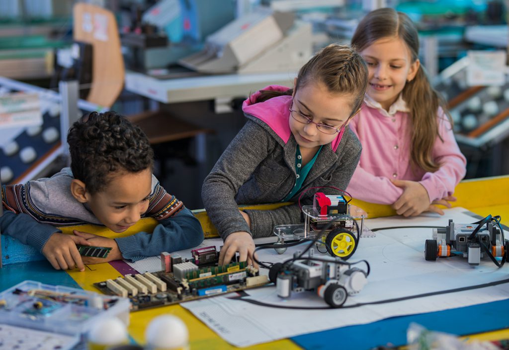 Group of small kids working on motherboard and robots in laboratory.