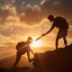 Male and female hikers climbing up mountain cliff and one of them giving helping hand.
