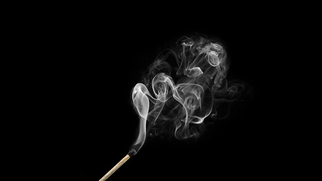 Burnt match with curls of smoke isolated on black