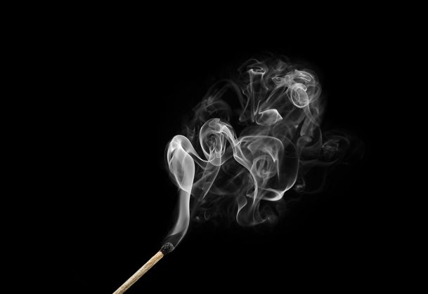 Burnt match with curls of smoke isolated on black