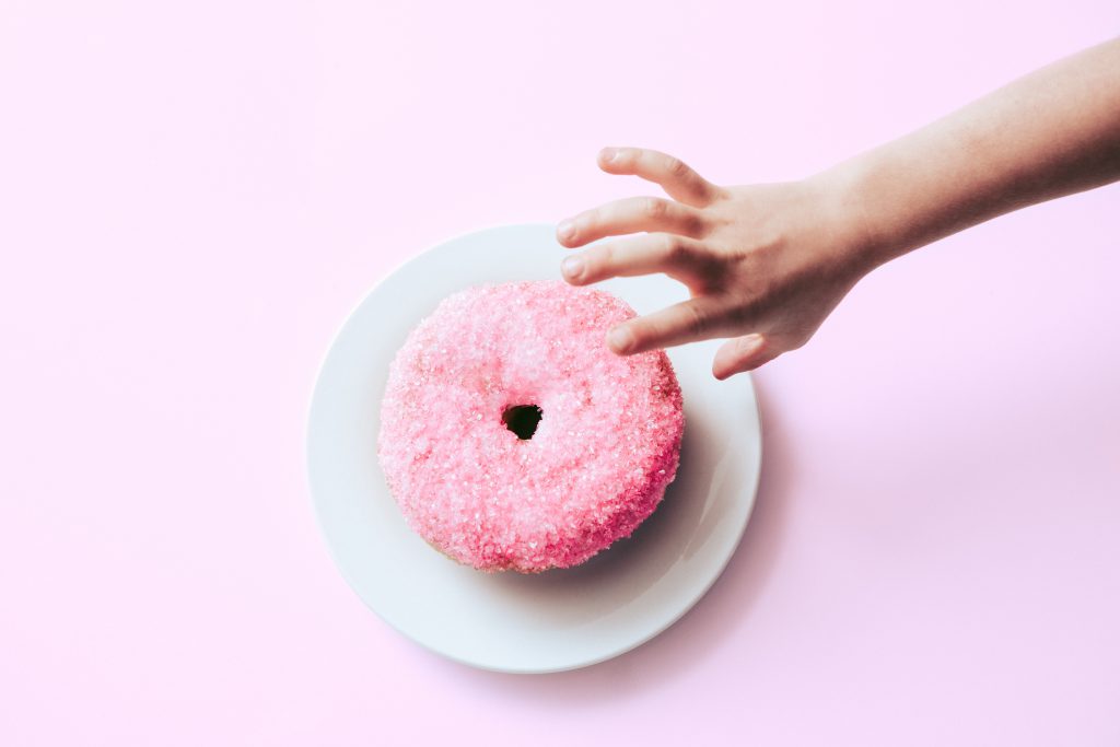 Child reaching for a pink donut with sprinkles