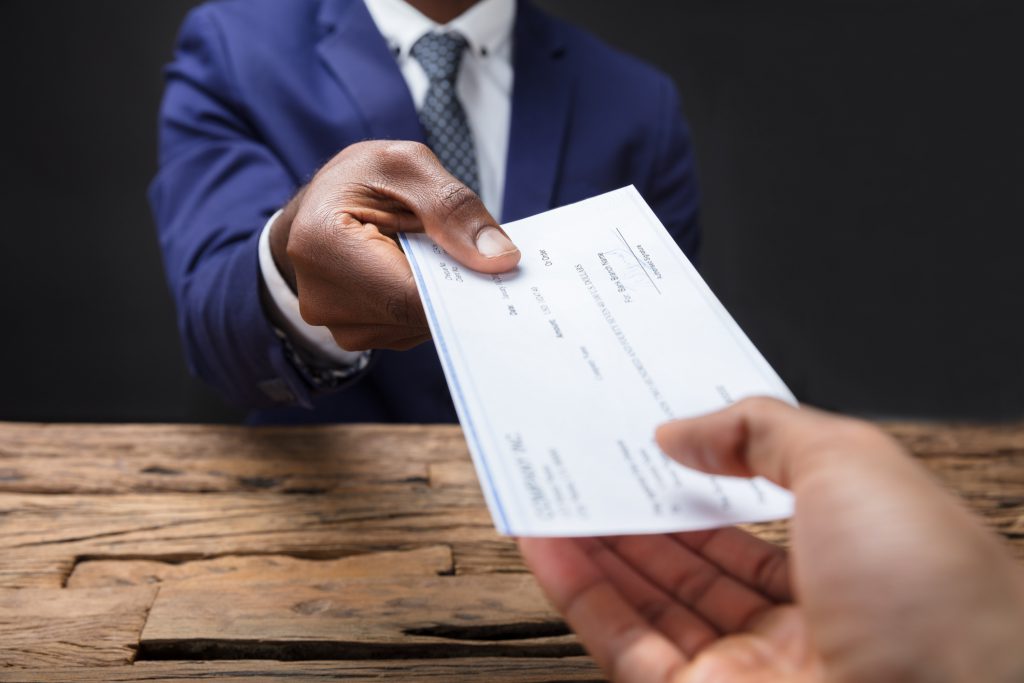 Businessperson hand passing over a check to another hand across a table