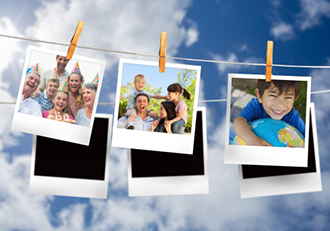 This is a photo of family photographs hanging on a clothesline in front of a cloudy sky.