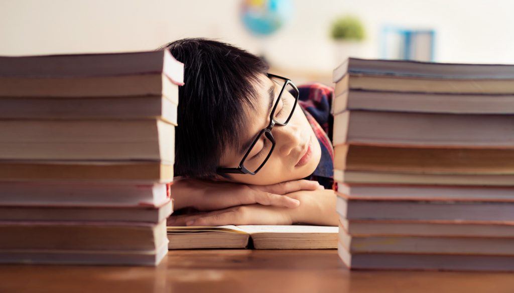 Student sleeping between piles of books