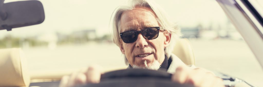 outdoor portrait of a modern senior man with long hair and beard driving a convertible classic car.