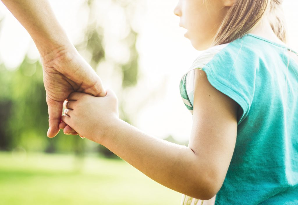 Mother is walking with her daughter in the park and holding hands..