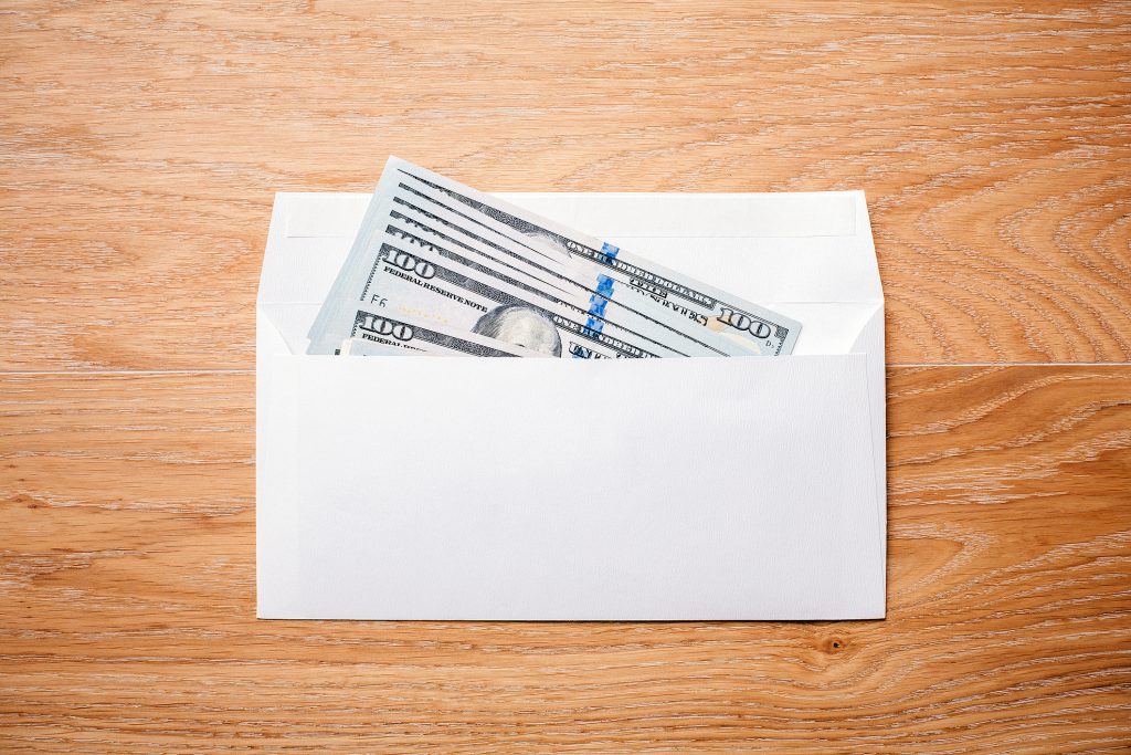 Top view of blank envelope with dollar banknotes on wooden desktop.