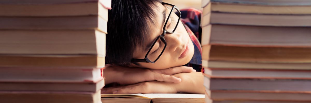 Student sleeping between piles of books