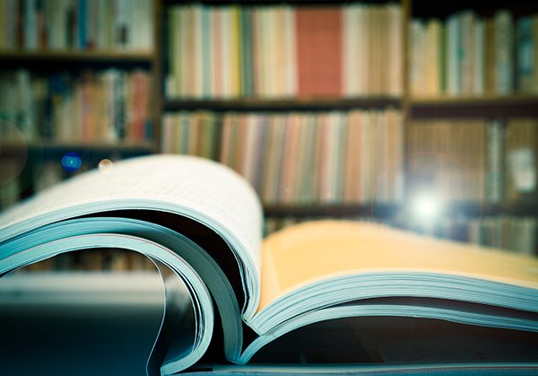 This is a photo of a pile of books and journals with a bookshelf in the background.