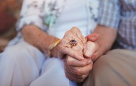 Cropped shot of elderly couple holding hands while sitting together at home.