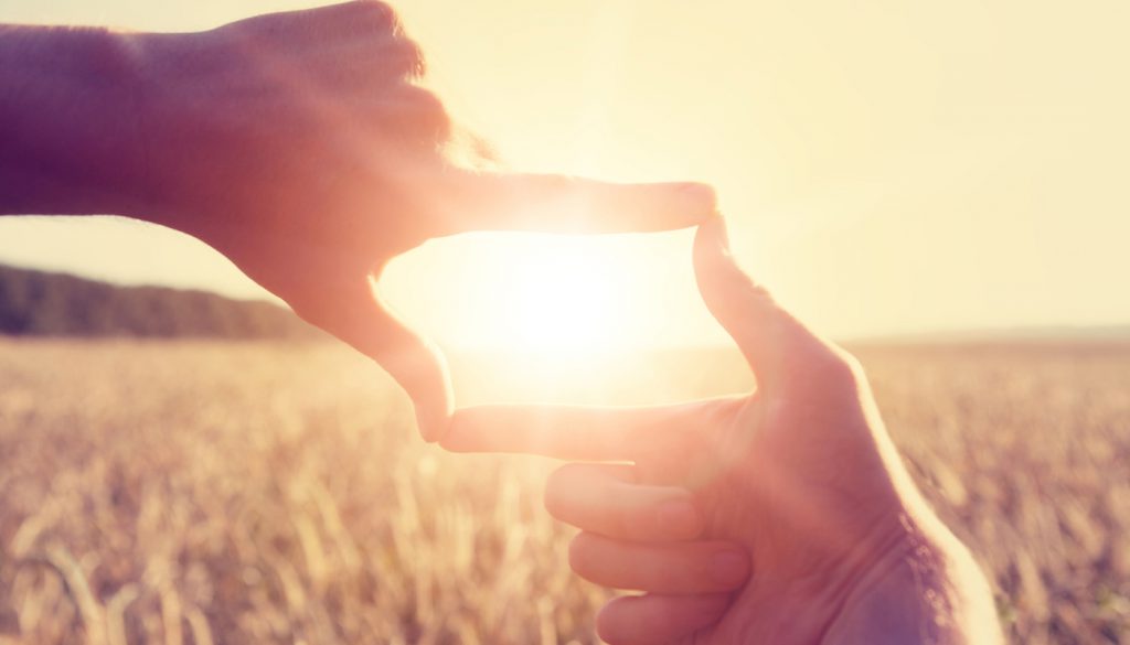 This is a photo of a woman using her hands to frame distant sun rays