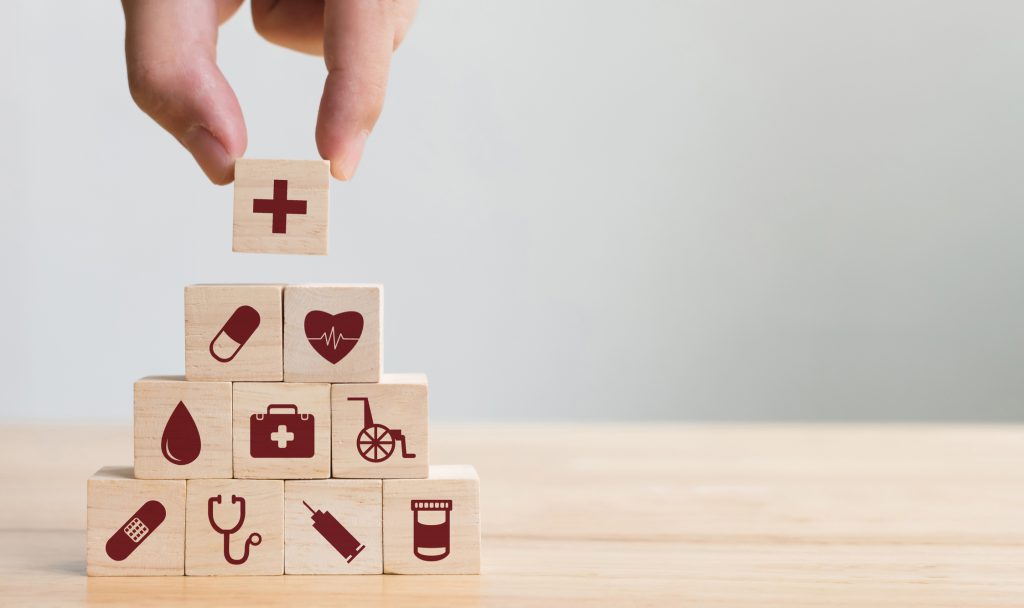 Hand placing wood blocks in a pyramid, each with a symbol representing health care and medicine