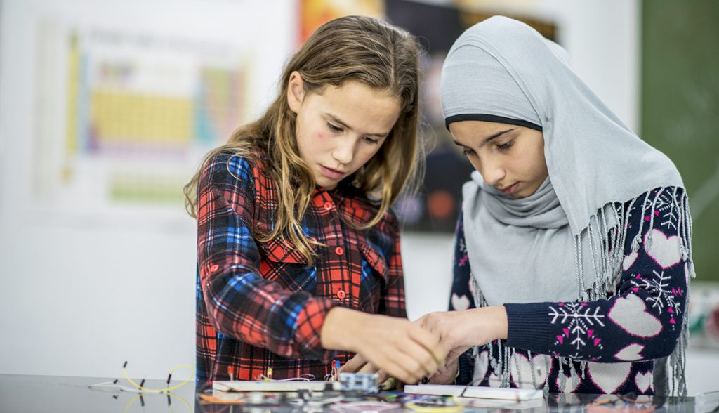 Two girls working together with wires and circuits during science class.