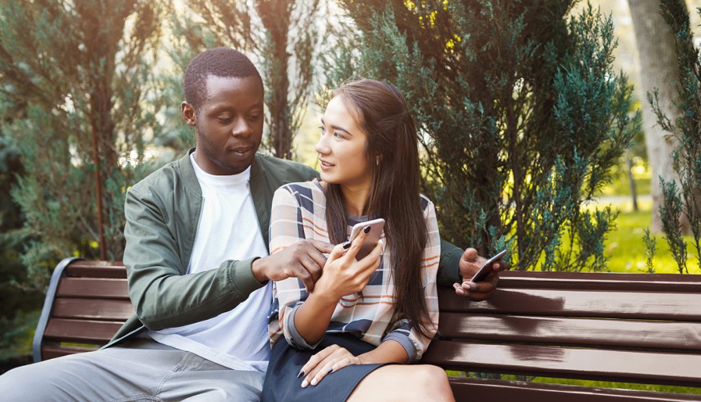 Couple looking at a phone sitting on a park bench