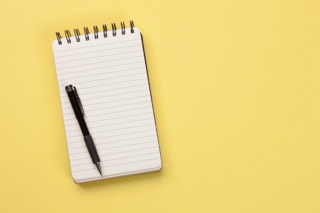 Blank lined notepad with a pen on a yellow surface