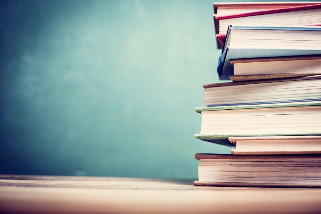 Textbooks on wooden school desk with chalkboard.