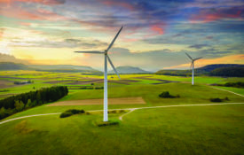 Aerial drone point of view of modern wind turbines in green rural landscape during a colorful sunset twilight. Green Energy, Alternative Energy Environment Concept Shot. Baden Württemberg, South Germany, Europe