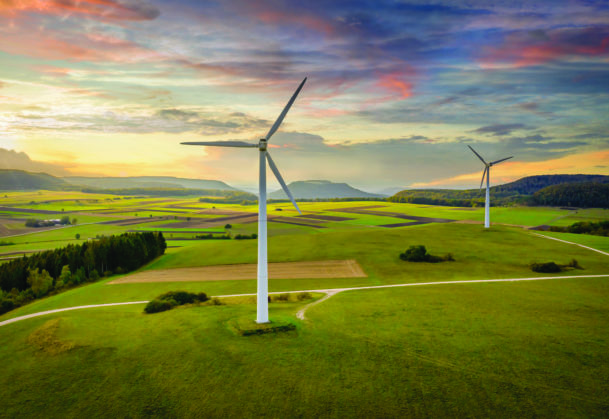 Aerial drone point of view of modern wind turbines in green rural landscape during a colorful sunset twilight. Green Energy, Alternative Energy Environment Concept Shot. Baden Württemberg, South Germany, Europe