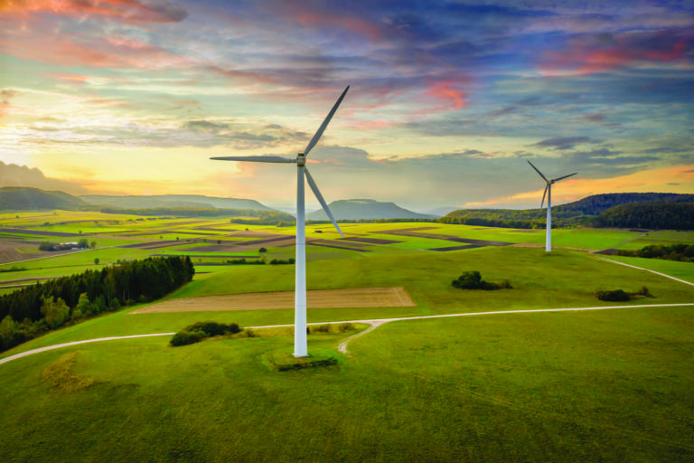 Aerial drone point of view of modern wind turbines in green rural landscape during a colorful sunset twilight. Green Energy, Alternative Energy Environment Concept Shot. Baden Württemberg, South Germany, Europe