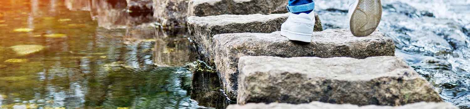 Photo of someone jumping on stepping stones across a body of water.