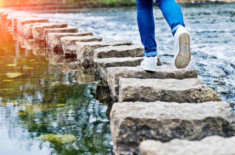 Photo of someone jumping on stepping stones across a body of water.