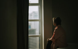 lonely senior woman standing in the dark looking out a window