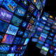 Multiple television screens in blue tones displaying the news.