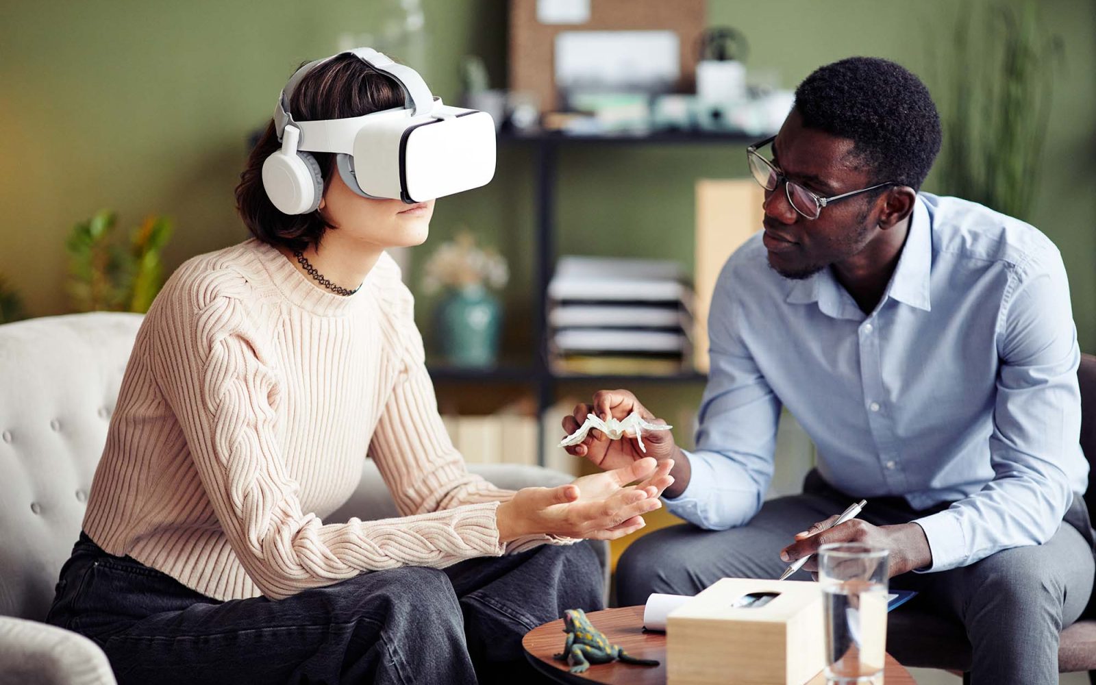 Software developer giving plastic spider to young woman wearing virtual reality headset.