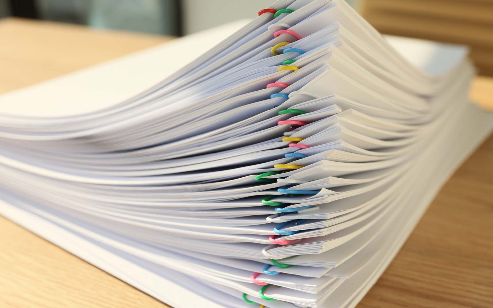 Closeup photo of a stack of documents with colorful paperclips separating each set.