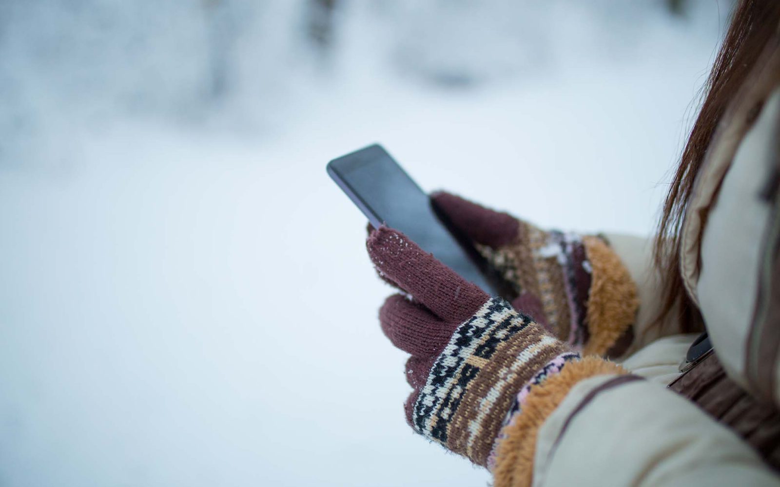 Female hands holding a cellphone outdoors in the snow.