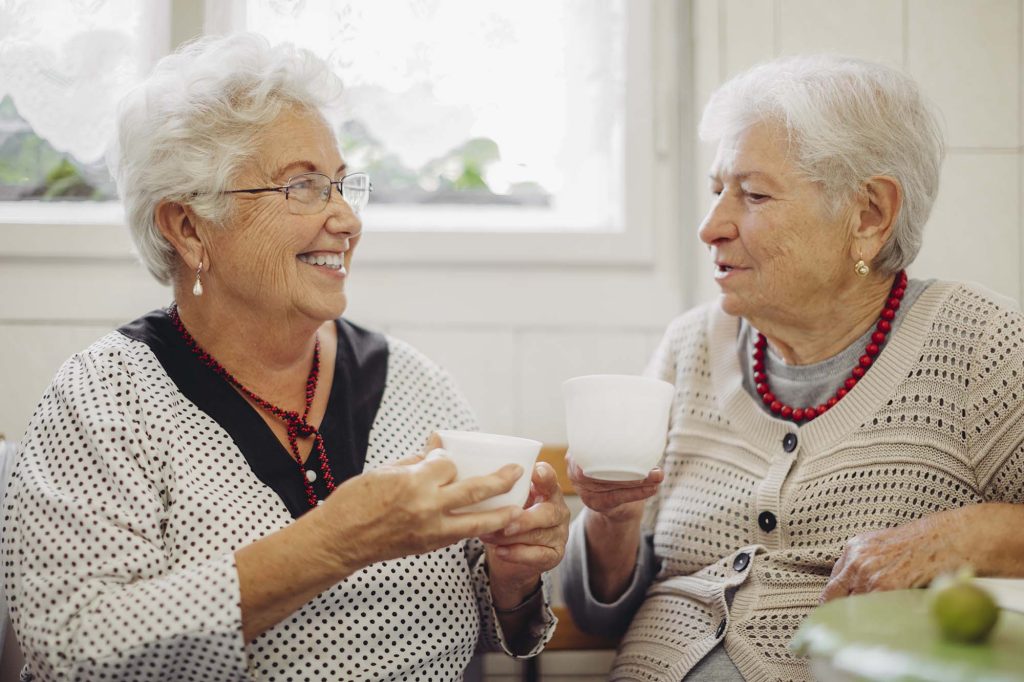 Two senior women holding mugs and talking to each other.