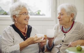 Two senior women holding mugs and talking to each other.